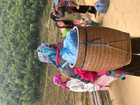       Local woman in colorful headscarf carries a woven basket while talking with trekkers in a rural mountain village.
  