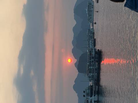       Orange sun setting behind limestone karsts with cruise boats reflecting on Halong Bay.
  