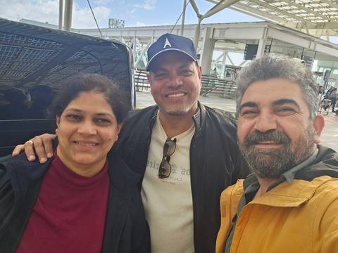       Smiling trio, including a local guide, take a close selfie outdoors near a transport terminal.
  