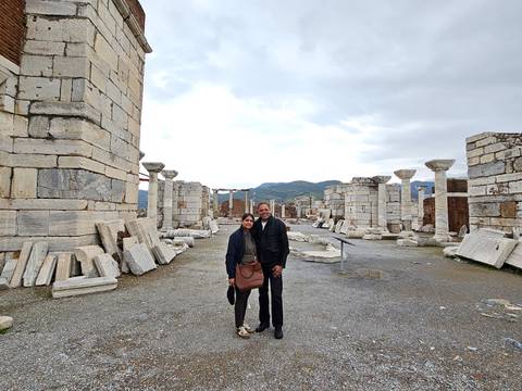       Two travellers stand amid scattered marble columns and ruins of an early Christian basilica.
  