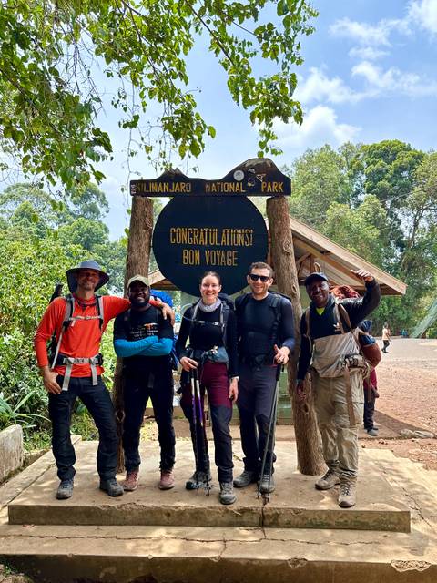       Group of trekkers celebrating at the Kilimanjaro National Park exit gate sign
  