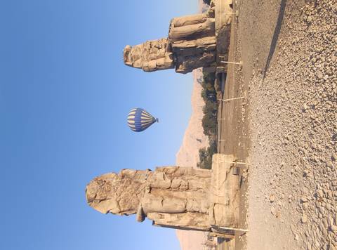       Hot-air balloon floating between the Colossi of Memnon in the early morning light.
  