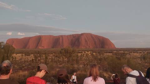       Tourists gathered at a viewpoint watching Uluru glow in the evening light
  
