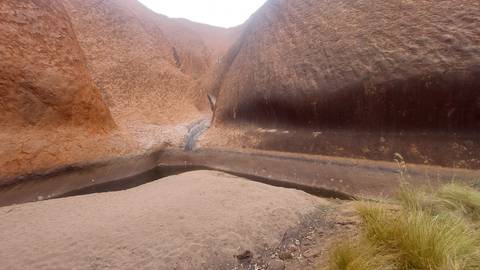       Shallow waterhole nestled between towering rust-red rock walls at Uluru
  