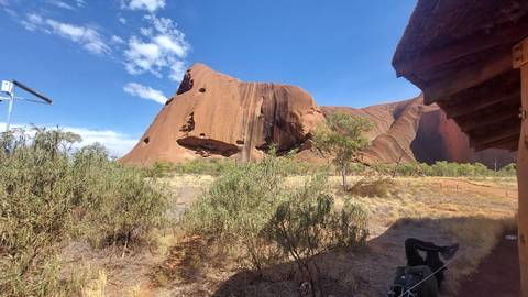       Side profile of Uluru’s sheer sandstone face rising above desert shrubs
  