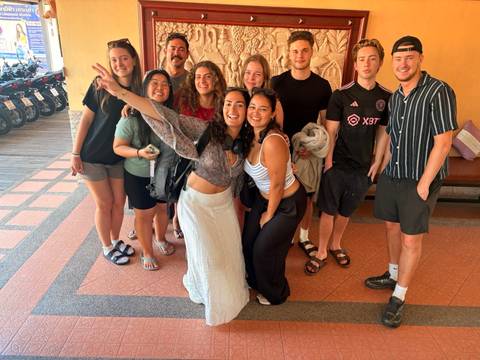       Smiling group of young travelers pose for a photo indoors before scooters lined up outside.
  