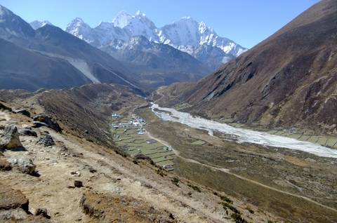       High-altitude vista of a Himalayan valley with clustered houses below snow-capped peaks.
  