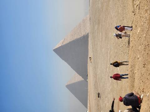       Tourists walking across the desert plateau in front of two of the Great Pyramids of Giza.
  