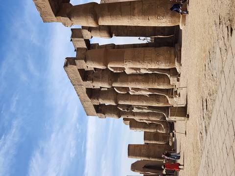       Row of towering sandstone columns with pharaonic statues in Luxor Temple courtyard.
  
