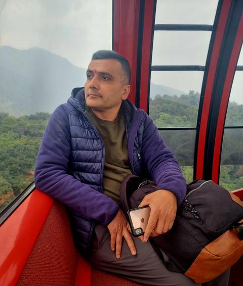       Man in a red cable-car cabin looks out over misty forested hills during an aerial ride.
  