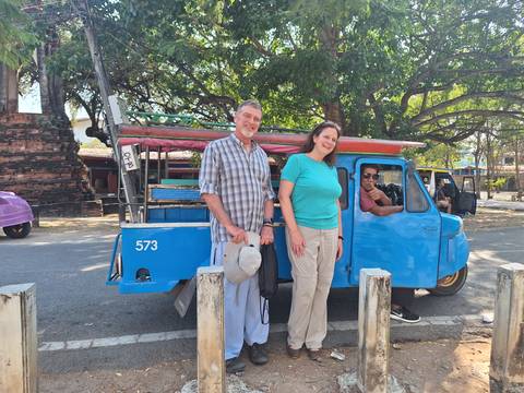       Smiling travellers stand beside a bright blue open-air tuk-tuk while the driver waits at the wheel.
  