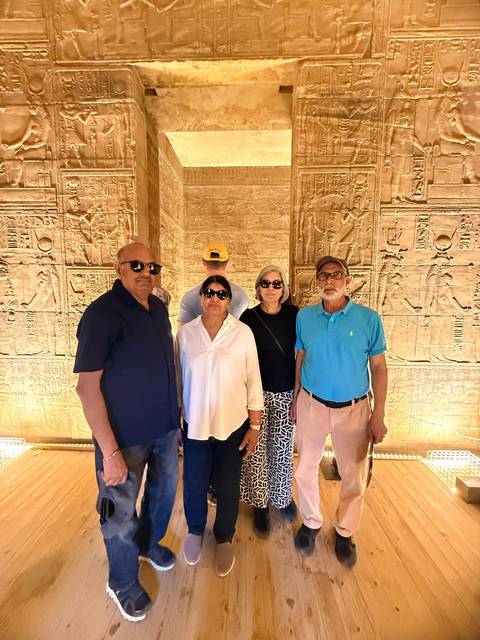       Travelers stand inside a hieroglyph-covered chamber illuminated with warm lighting.
  