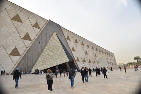       Facade of the new Grand Egyptian Museum with pyramid-shaped entrance and visitors outside.
  