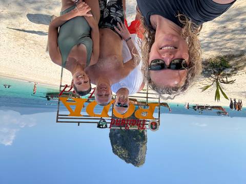       Four friends take a selfie on white-sand Poda Island beach with turquoise water and a limestone stack behind.
  