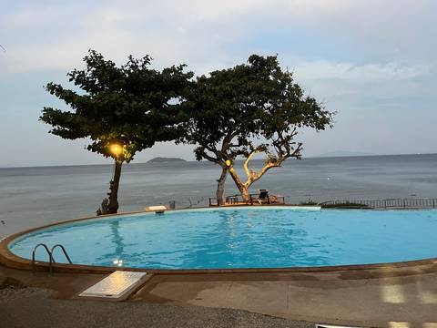       A tranquil infinity pool overlooks the sea and a small island as evening lights glow in surrounding trees.
  