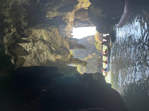       Tourists paddling inflatable kayaks through a dramatic limestone sea cave with sunlight streaming from the exit.
  