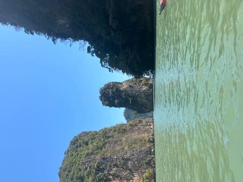       Tall limestone karst island rising from turquoise water under a clear blue sky.
  