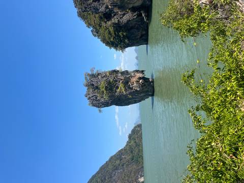       Iconic needle-shaped rock stack standing alone in a green bay framed by jungle-covered cliffs.
  