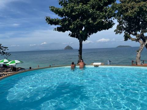      Couple relaxing in an infinity pool overlooking a calm tropical sea and distant islands.
  