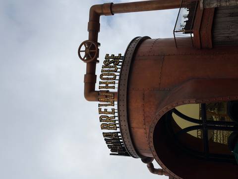       Copper-toned industrial style facade with sign reading 'BANA BREW HOUSE' under cloudy skies.
  