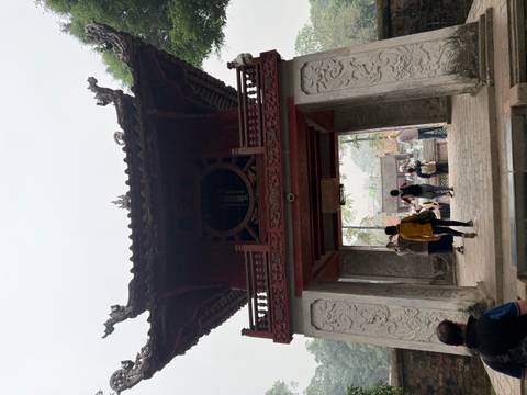       Stone gateway with ornate dragons at the Temple of Literature as visitors walk underneath.
  