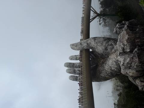       Spectacular Golden Bridge held by giant stone hand amid misty mountains with crowds strolling across.
  
