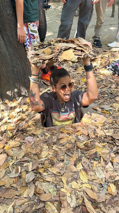       Excited visitor emerging from a narrow Cu Chi tunnel hatch amid dry leaves.
  
