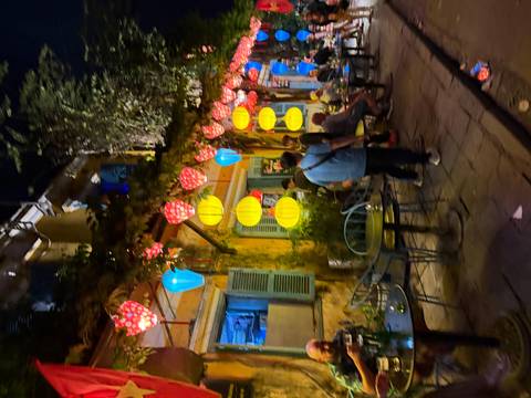       Night street scene in Hoi An with colorful lanterns and blurred pedestrians outside cafes.
  