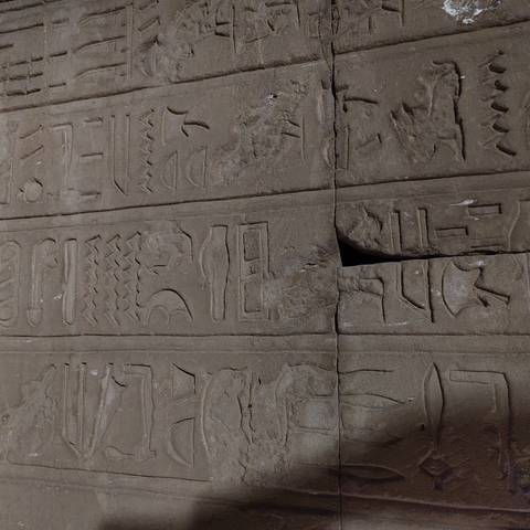       Close-up of ancient Egyptian hieroglyphs carved into weathered stone blocks.
  