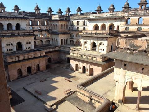       Interior courtyard of Orchha Fort palace complex with tiered arcades and open chambers lit by sun.
  