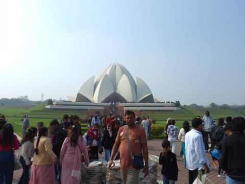       Crowds of visitors walk up a wide path toward the white Lotus Temple set amid green lawns under a clear sky.
  