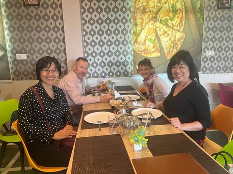       A group of diners sit around a wooden table in a casual restaurant, ready to enjoy an Indian meal.
  