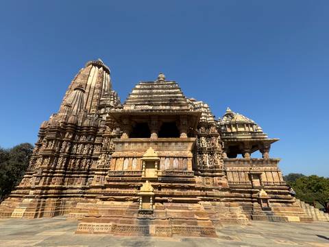       Well-preserved sandstone temple with ornate sculptures rises sharply against a clear blue sky.
  