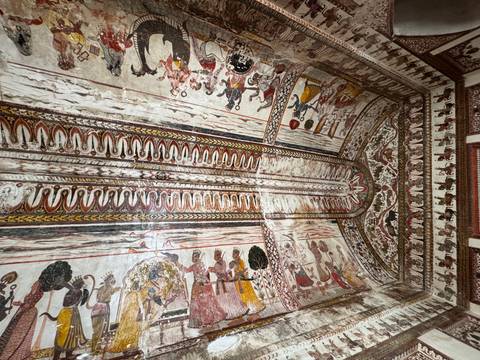       Ceiling fresco richly painted with historic scenes and geometric patterns inside an Indian palace.
  