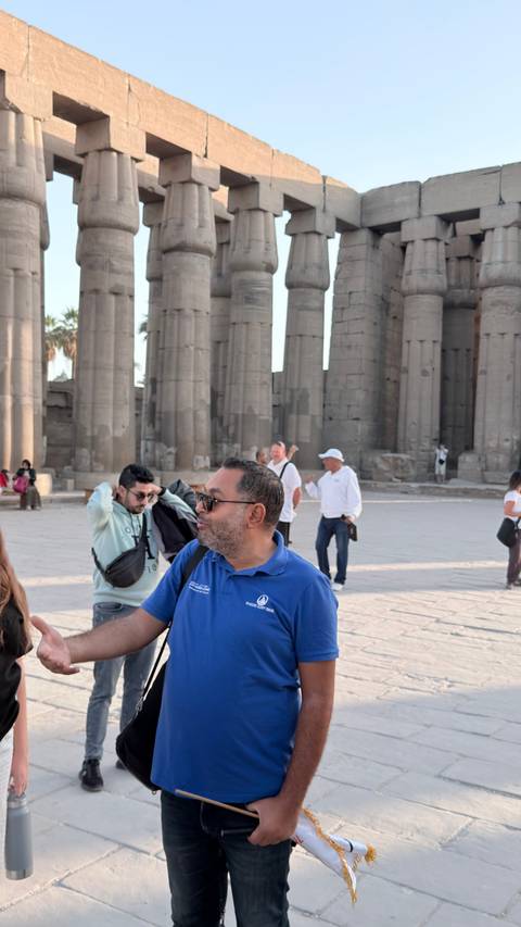      Visitors mill about the spacious courtyard of Luxor Temple amid towering stone columns.
  