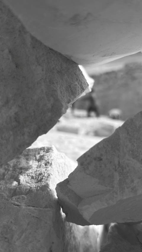       Out-of-focus black-and-white shot looking through a gap between ancient stones.
  