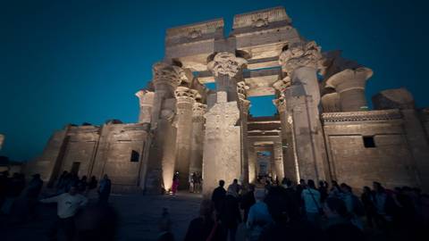       Nighttime visit to Kom Ombo Temple where spotlights illuminate the massive columns against a deep blue sky as visitors walk below.
  