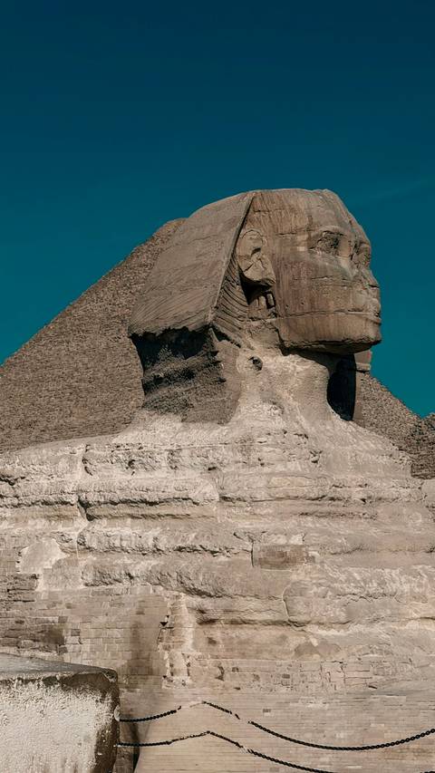       Close side profile of the Sphinx with a pyramid backdrop against deep blue sky
  