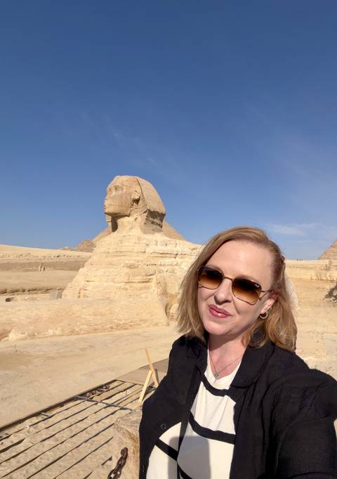       Woman takes selfie smiling in front of the Sphinx on a bright day
  