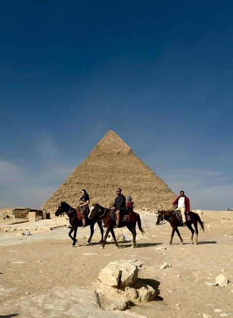       Three riders on horses pose before the Great Pyramid under clear blue sky
  