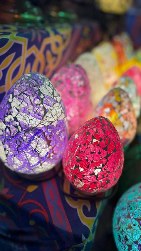       Vibrant mosaic glass eggs in shades of purple, pink and red on market display
  