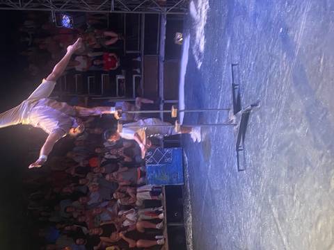       Acrobat performing a balancing act on poles in a dimly lit circus arena before an audience
  