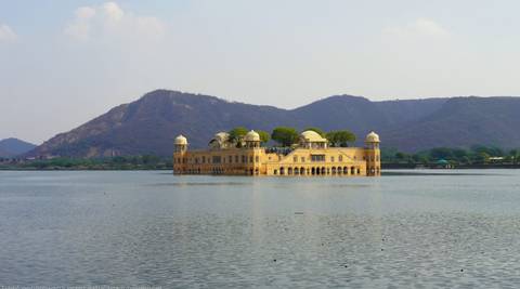       Jal Mahal palace sitting serenely in the middle of Man Sagar Lake with hills rising behind
  
