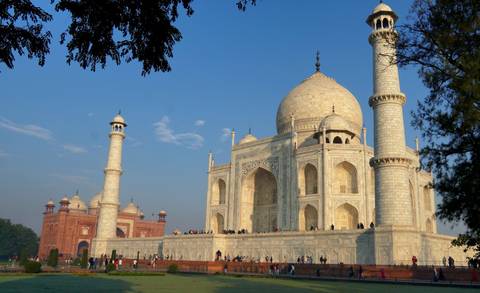       The white marble Taj Mahal gleams under a clear blue sky with visitors at its base.
  