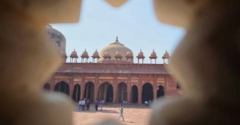       A Mughal courtyard and domes are viewed creatively through a star-shaped lattice window.
  