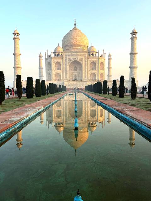       Perfect reflection of the Taj Mahal in the long central pool framed by cypress trees at dawn.
  
