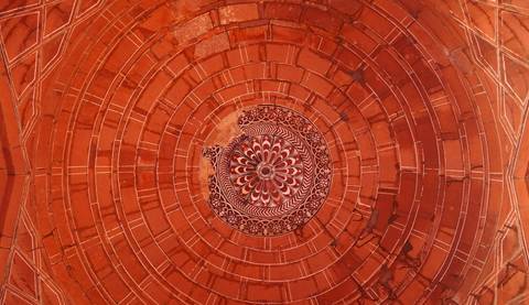       Detailed concentric design in red sandstone ceiling with floral centerpiece at Agra monument.
  