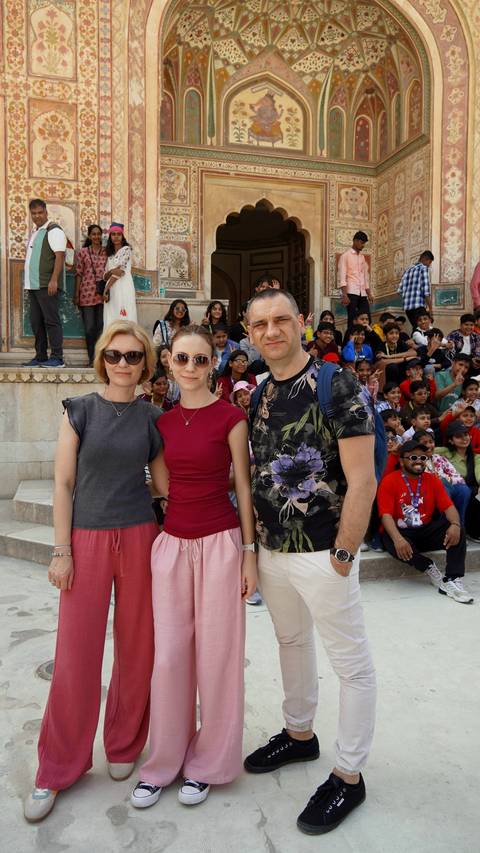       Family portrait with a lively crowd of school children in the background at an Indian monument.
  