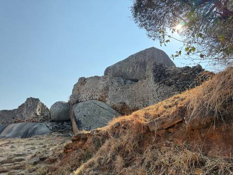       Ancient stone ruins and massive boulders on a hilltop under a bright blue sky.
  