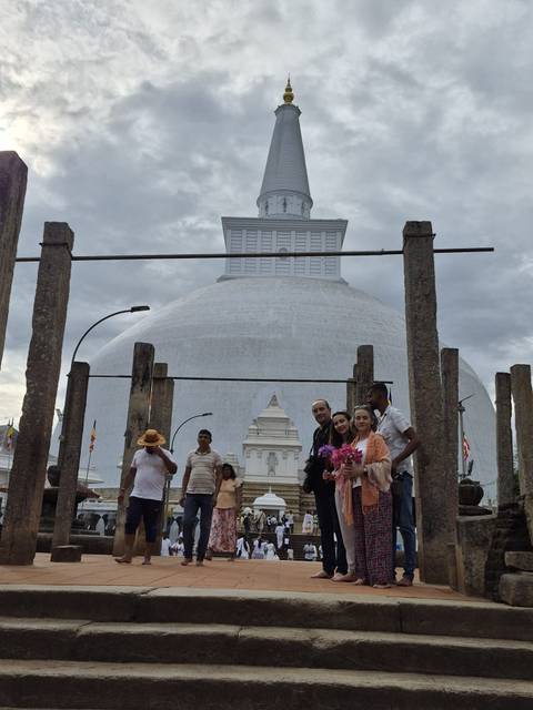       Visitors stand between stone pillars with a massive white dagoba in the background.
  